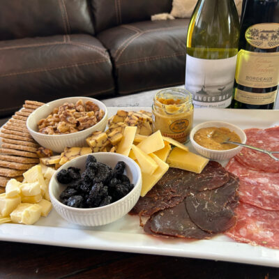Meats, cheeses and crackers from an AppyHour subscription box sitting on a tray with two wine bottles in the back