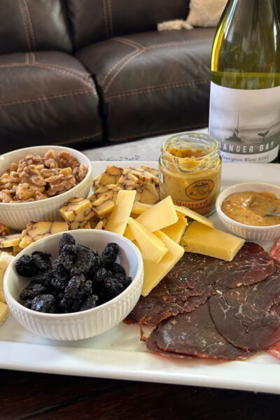 Meats, cheeses and crackers from an AppyHour subscription box sitting on a tray with two wine bottles in the back