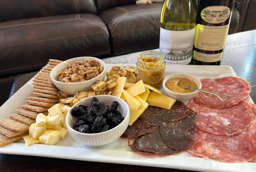 Meats, cheeses and crackers from an AppyHour subscription box sitting on a tray with two wine bottles in the back